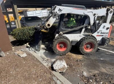 Bobcat machinery breaking concrete on a parking lot.